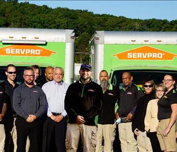 Full SERVPRO office staff and production crew. Smiling employees standing in front of SERVPRO trucks.