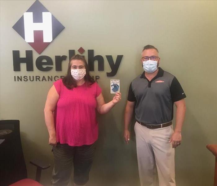 Prize winner, woman receiving giftcard from SERVPRO employee in front of Herlihy sign.
