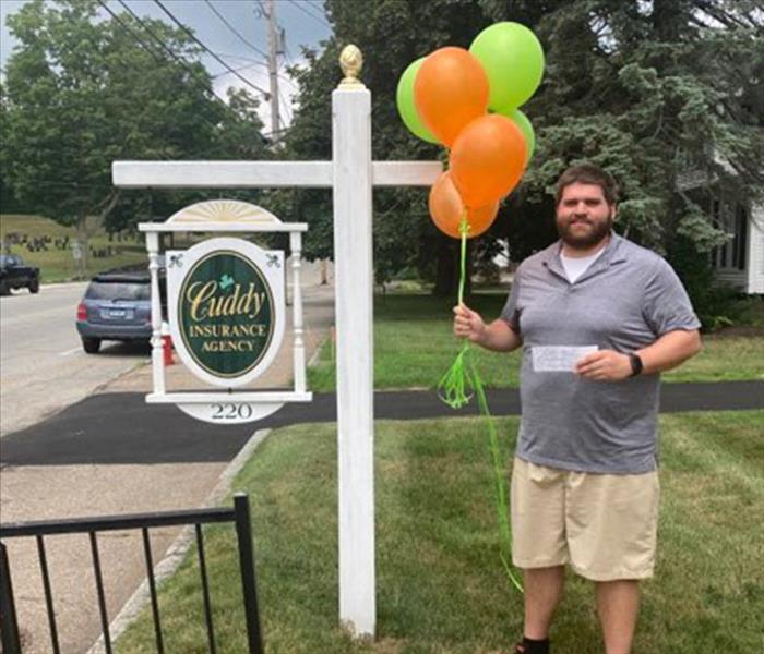 Prize Winner- Man holding Balloons in front of Cuddy Insurance Sign