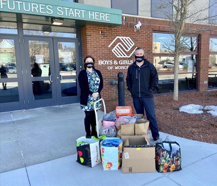 Man and woman standing outside Boys Club front doors with  bags and boxes of food for donation